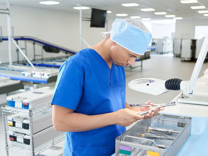 A male healthcare professional is inspecting surgical instruments in sterile container systems