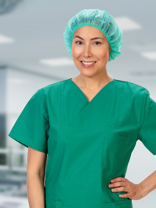A female healthcare professional stands in  in green scrubs, smiling