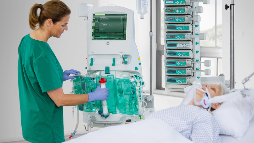 A patient is in bed and connected to the dialysis machine. The nurse operates the machine.