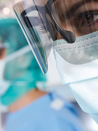 Female doctor wearing a mask and special glasses, looking concerned as she observes a procedure