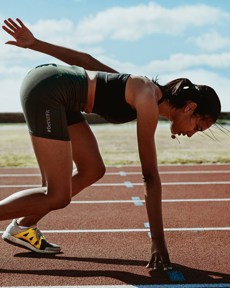 A female runner is standing on the start line, with her body slightly bent forward and her feet positioned to push off quickly