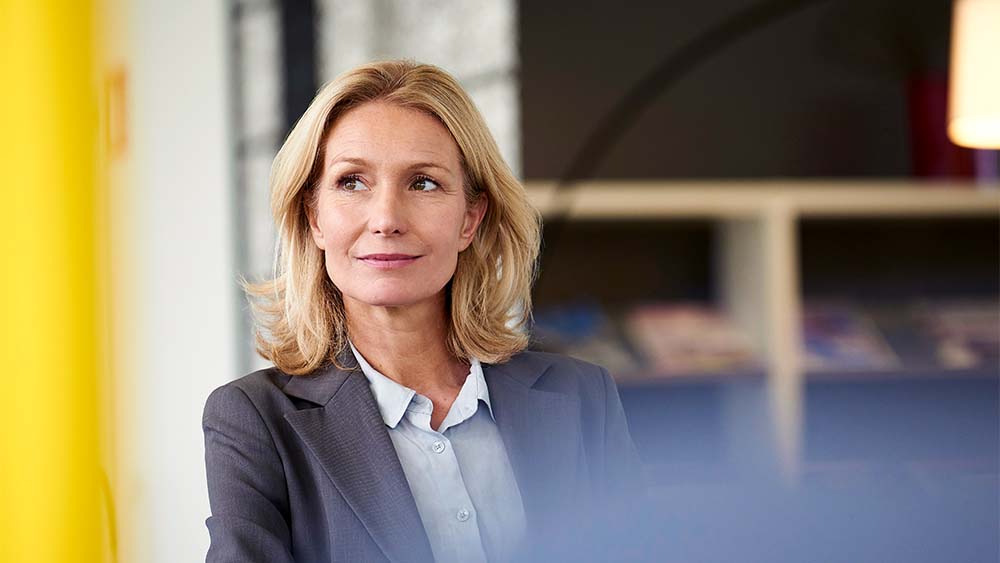 Confident woman in a grey suit looks past the camera.  